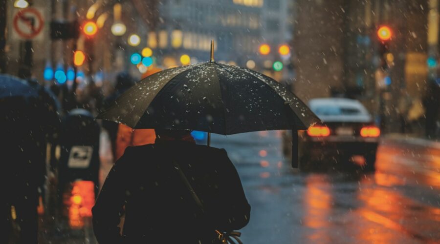 person walking on street and holding umbrella while raining with vehicle nearby