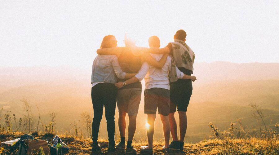 four person hands wrap around shoulders while looking at sunset
